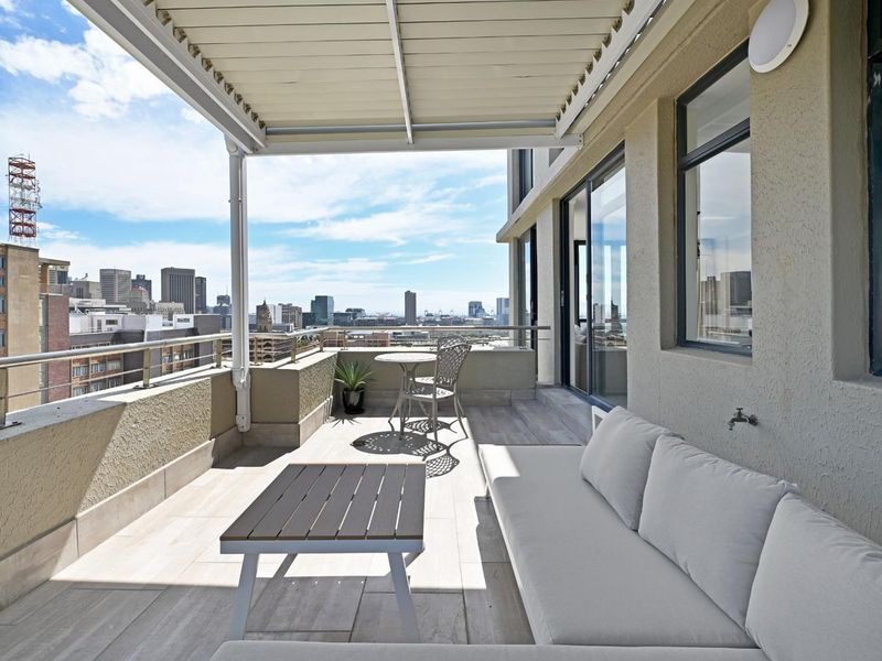 Spacious apartment balcony featuring tiled flooring, a retractable awning, and metal railings, offering expansive city skyline views.