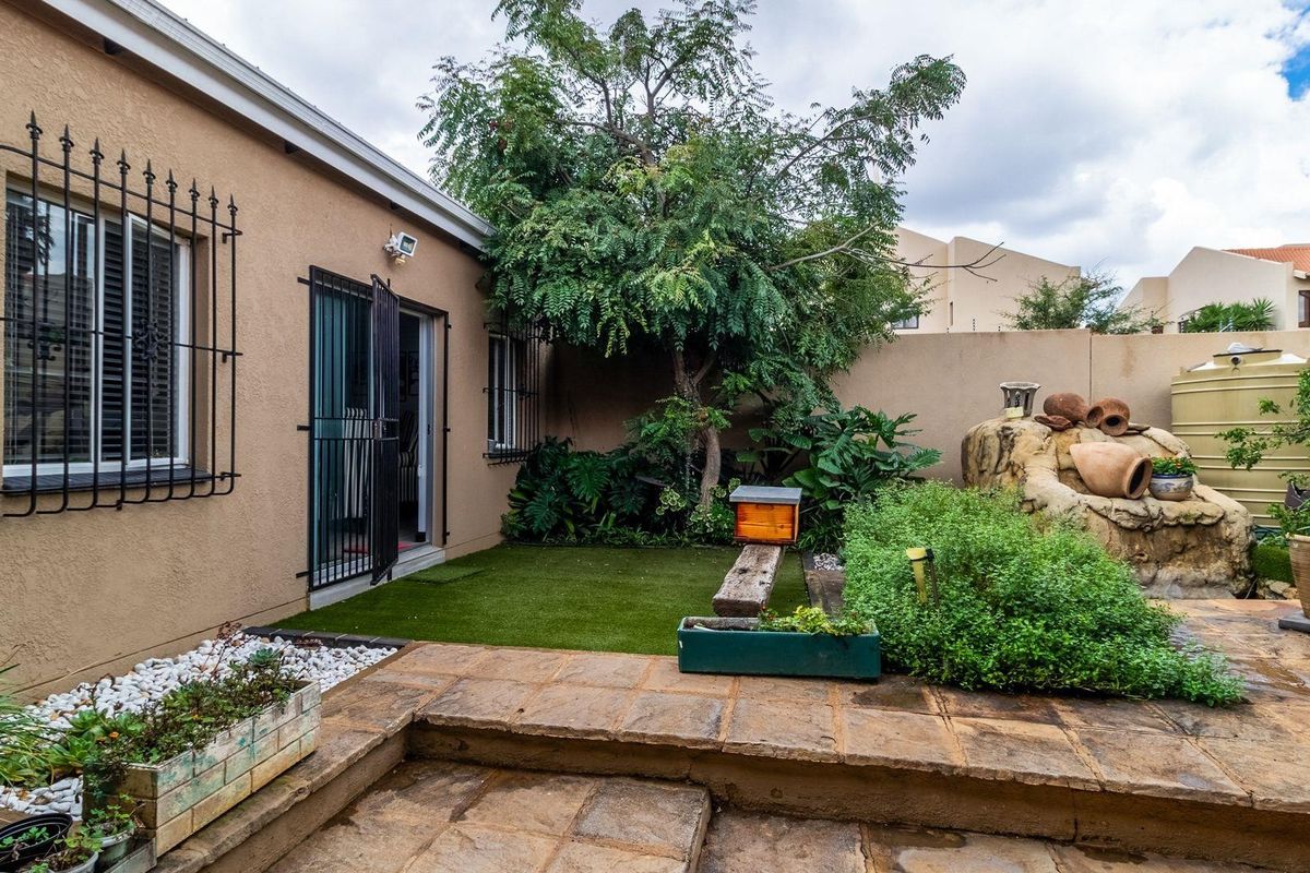 A private rear courtyard featuring stone paving, artificial lawn, established greenery, and a built-in water feature, providing a low-maintenance outdoor living space.