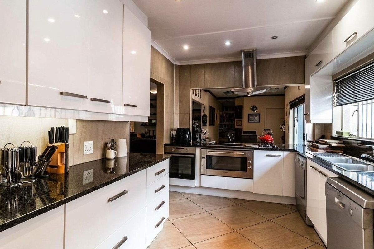 Modern kitchen featuring white high-gloss cabinetry, dark granite countertops, built-in stainless steel appliances, and tiled flooring with recessed lighting.