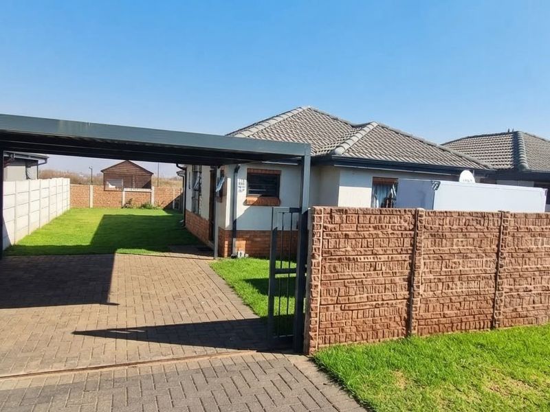 Front exterior view featuring a paved driveway, covered carport, and secure boundary walling with a well-maintained lawn.