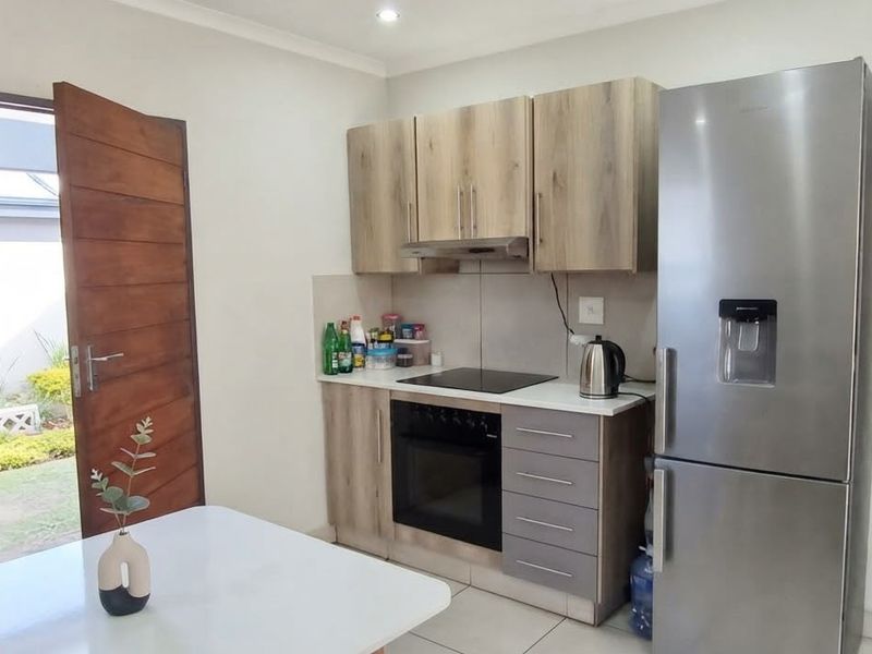Compact kitchen featuring modern wood-look cabinetry, built-in oven and hob, extractor fan, and tiled flooring with direct access to the exterior.