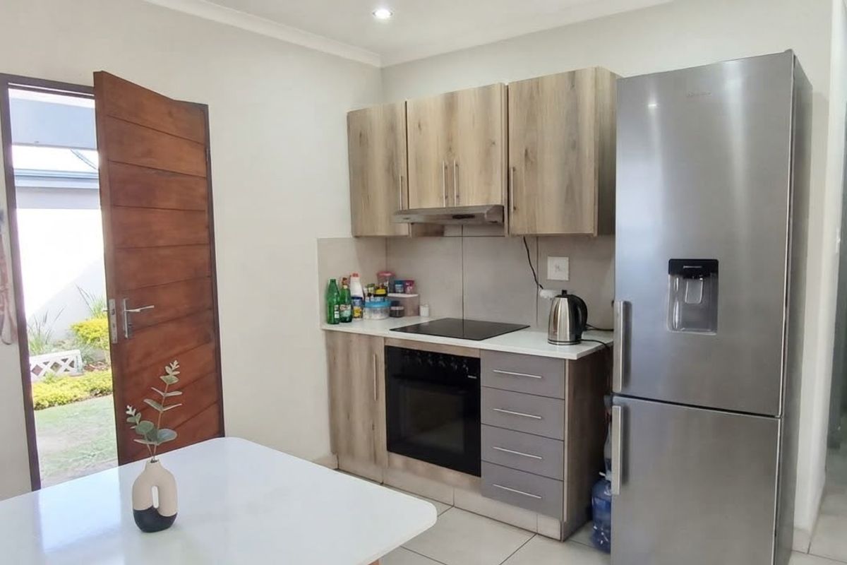 Compact kitchen featuring modern wood-look cabinetry, built-in oven and hob, extractor fan, and tiled flooring with direct access to the exterior.