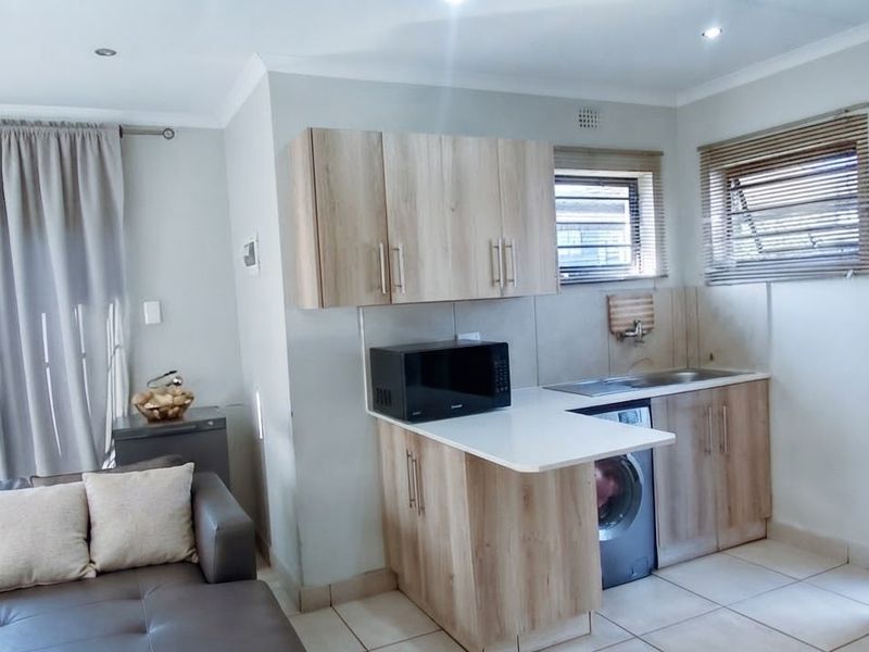 Open-plan living area featuring a compact kitchen with laminate cabinetry, stone-look countertops, and tiled flooring, seamlessly integrated with the adjacent living space.