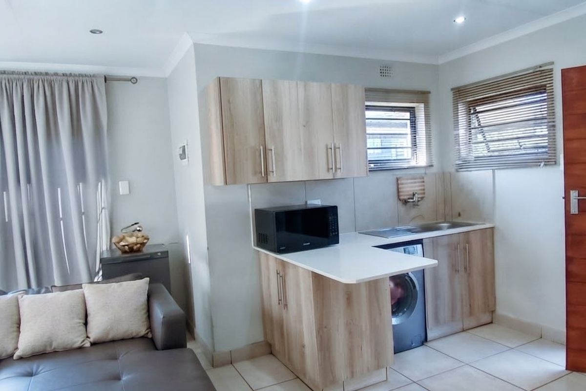 Open-plan living area featuring a compact kitchen with laminate cabinetry, stone-look countertops, and tiled flooring, seamlessly integrated with the adjacent living space.