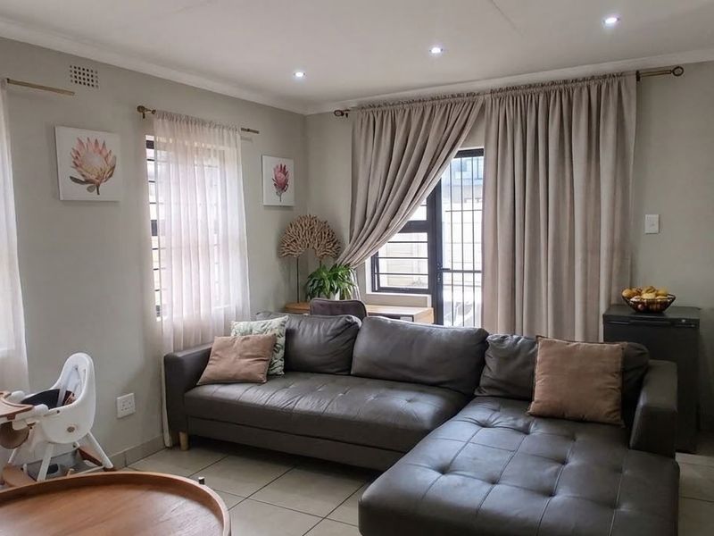An open-plan living area featuring tiled floors, recessed downlights, and direct access to an outdoor space through a security gate.
