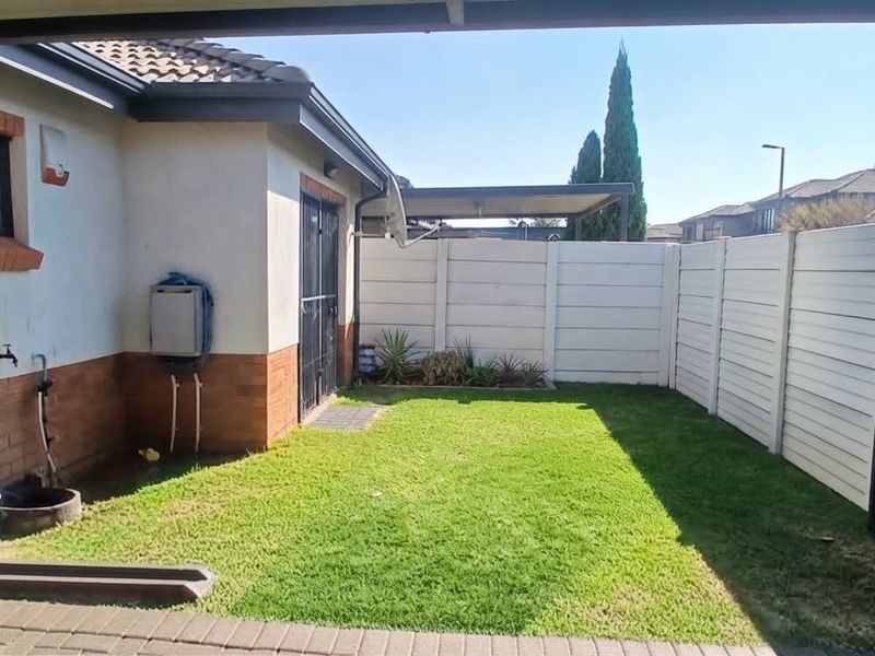 A private rear garden area featuring a small lawn, paved patio, and secure perimeter walling with a brick and plaster exterior finish.