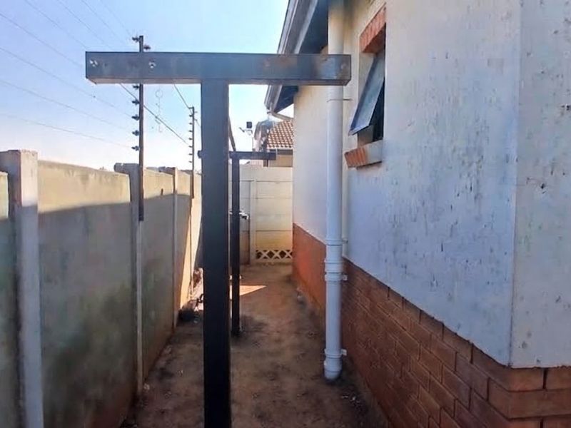 Side exterior area featuring a precast boundary wall with electric fencing, metal washing line poles, and a brick and plaster facade.