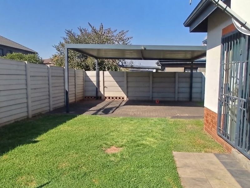 Rear garden area featuring a paved driveway, metal carport structure, and secure precast concrete boundary walls.