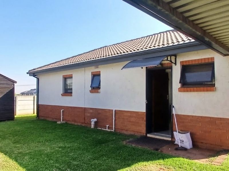 Rear view of the property featuring a brick and plaster facade, tiled roof, and a detached garden shed set within a grassed yard.
