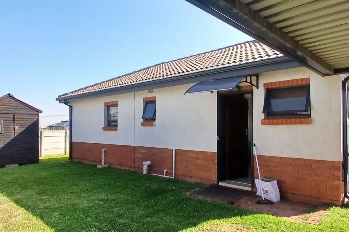Rear view of the property featuring a brick and plaster facade, tiled roof, and a detached garden shed set within a grassed yard.