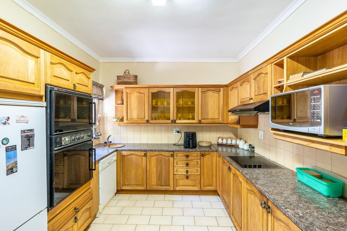 A functional kitchen featuring traditional wooden cabinetry, laminate countertops, built-in oven, hob, and extractor fan with tiled flooring and backsplash.