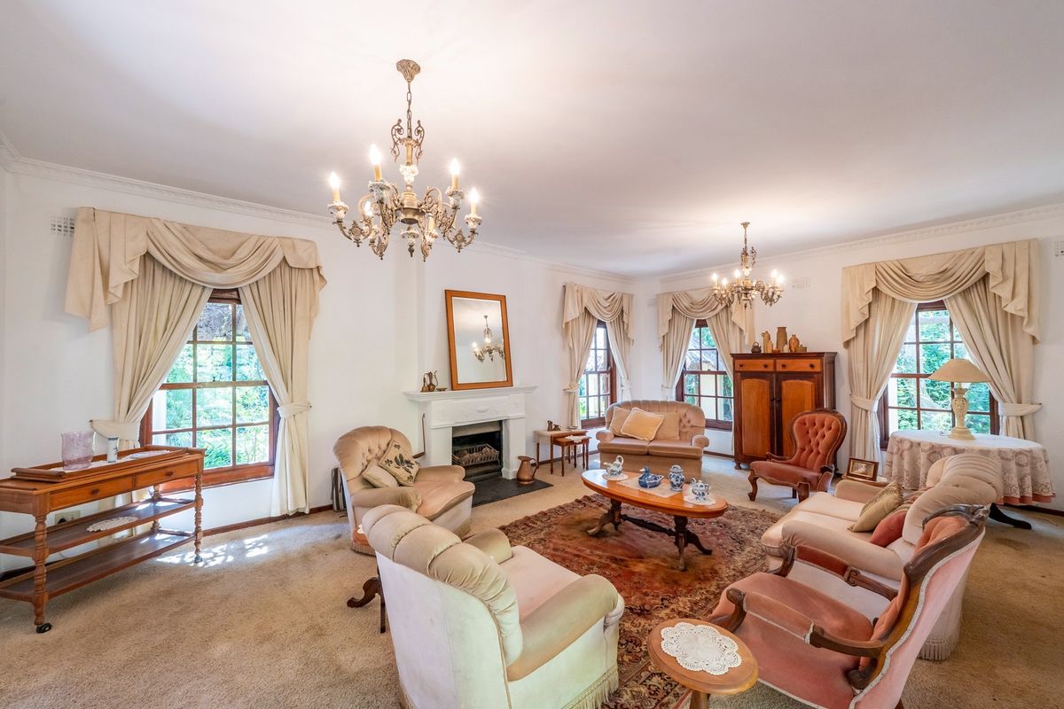 Spacious living room featuring a classic fireplace, ornate chandeliers, and large timber-framed windows with traditional drapery.