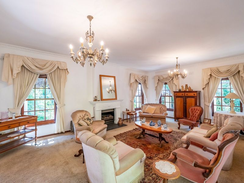 Spacious living room featuring a classic fireplace, ornate chandeliers, and large timber-framed windows with traditional drapery.