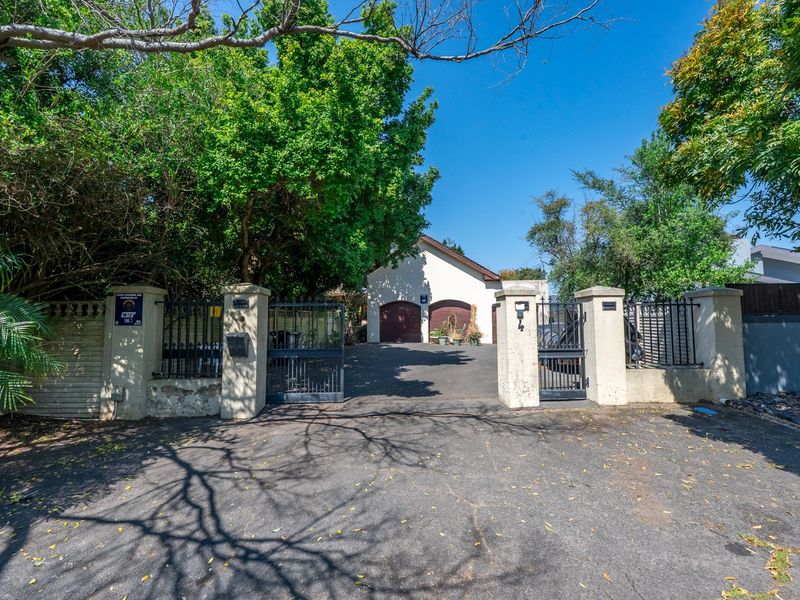 Front entrance view featuring a paved driveway, secure metal gates, perimeter walling, and a double garage structure.