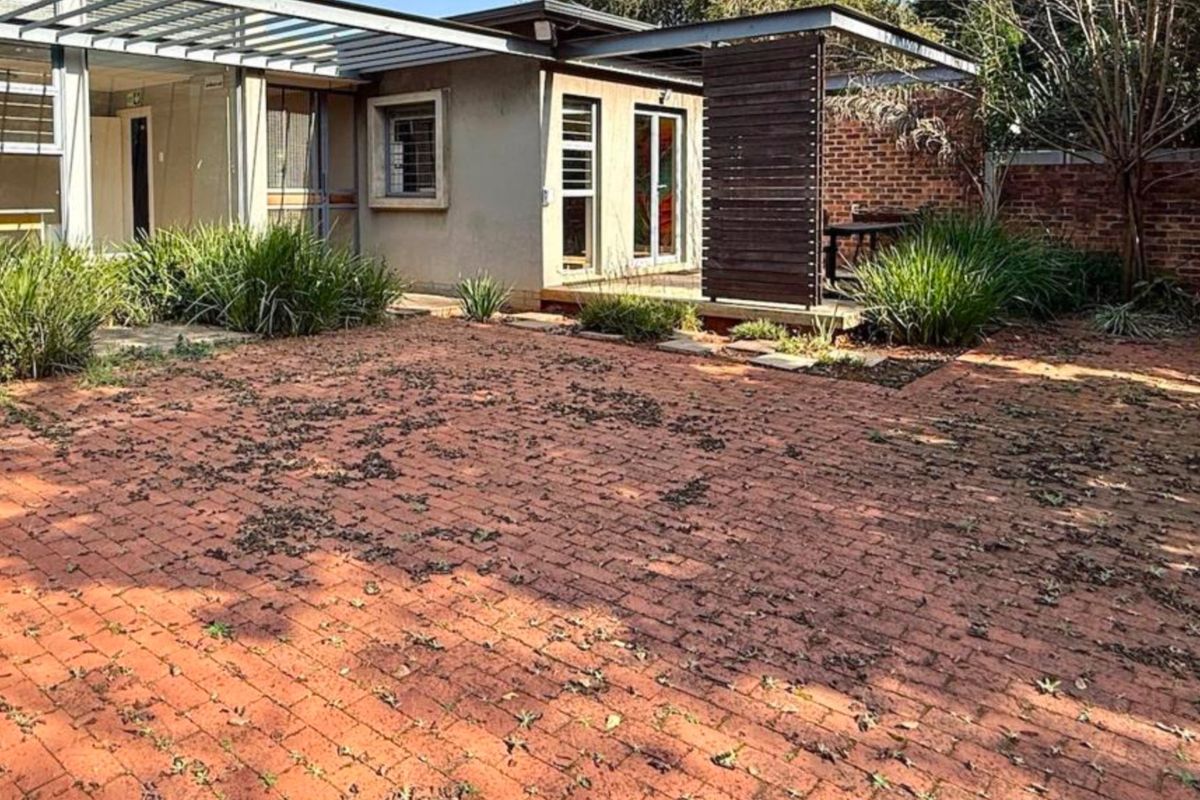 A rear exterior view featuring a brick-paved courtyard, a pergola structure, and a timber privacy screen, providing a functional outdoor living space.