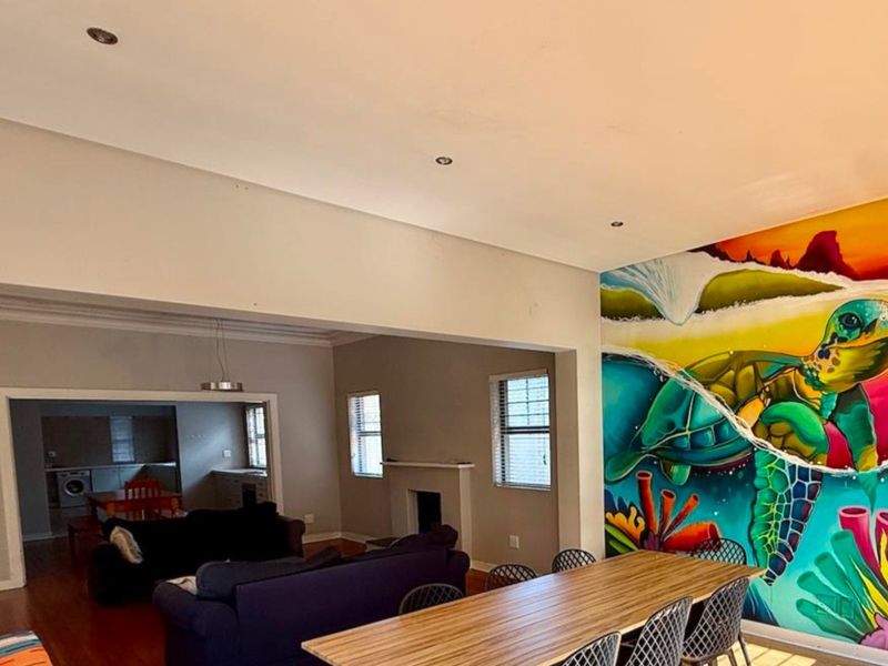 Spacious open-plan living and dining area featuring a prominent feature wall mural, recessed lighting, and a fireplace, connecting to an adjacent kitchen space.