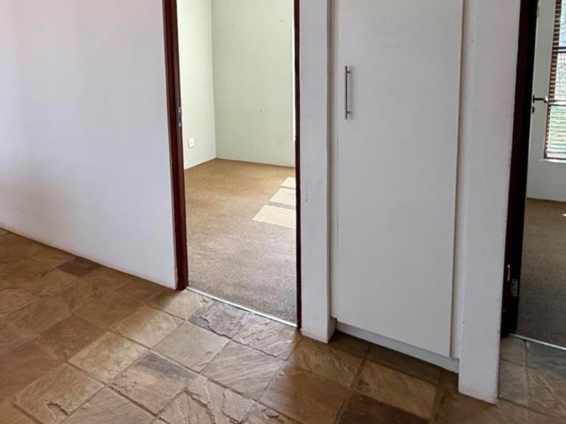 A functional hallway area featuring tiled flooring, a built-in storage cupboard, and access to adjacent carpeted rooms.