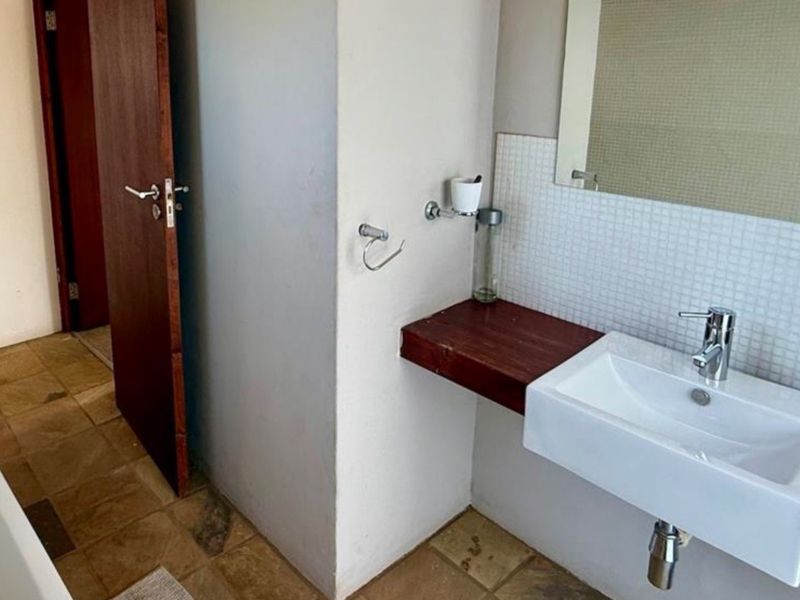 A functional bathroom featuring a wall-mounted basin with a wooden vanity shelf, a bathtub with a glass screen, and tiled flooring.