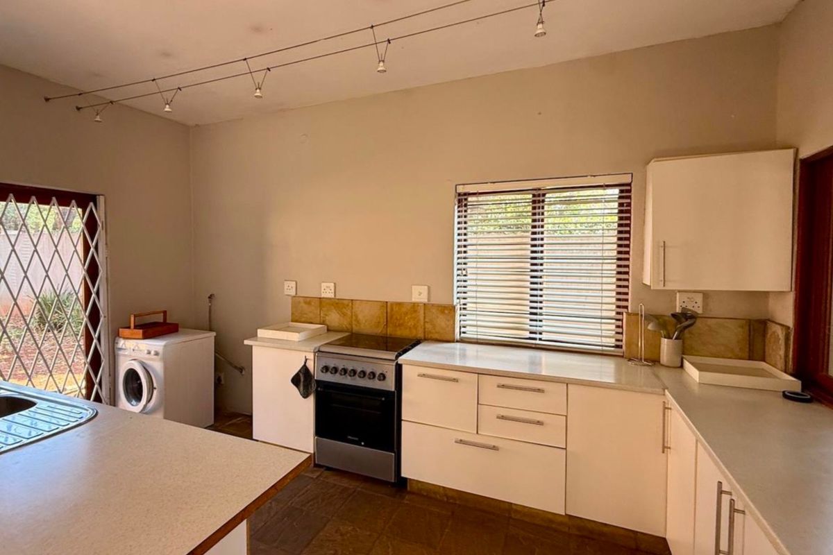 Functional kitchen featuring white cabinetry, laminate countertops, tiled splashback, and a freestanding stove, with direct access to the exterior via a security gate.
