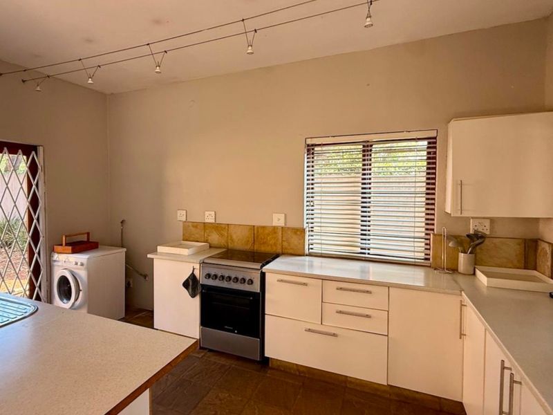 Functional kitchen featuring white cabinetry, laminate countertops, tiled splashback, and a freestanding stove, with direct access to the exterior via a security gate.