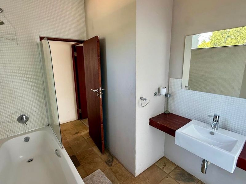 A functional bathroom featuring a bathtub with shower attachment, glass screen, and a wall-mounted basin with a wooden vanity shelf.