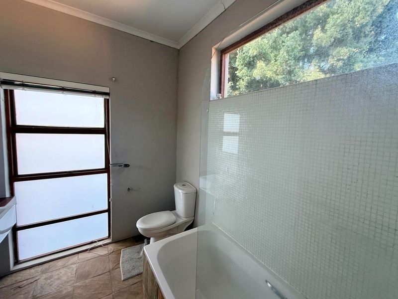 A functional bathroom featuring a bathtub with a glass screen, a toilet, and frosted windows, requiring some cosmetic updates to the flooring and finishes.