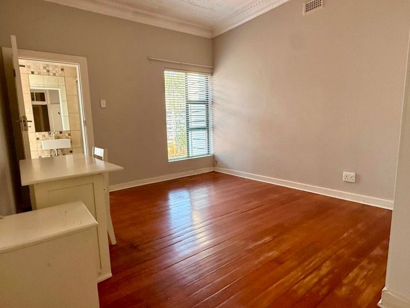 A bright, empty bedroom featuring polished hardwood flooring, decorative cornice, and an adjoining en-suite bathroom.