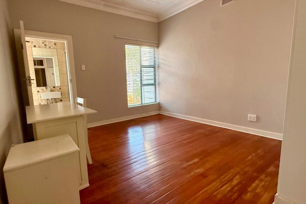 A bright, empty bedroom featuring polished hardwood flooring, decorative cornice, and an adjoining en-suite bathroom.