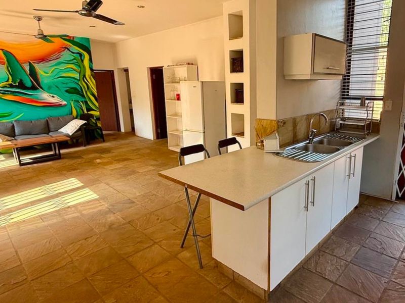 Open-plan living area featuring stone tile flooring, a functional kitchen with built-in cabinetry, and a ceiling fan, creating a versatile and connected living space.