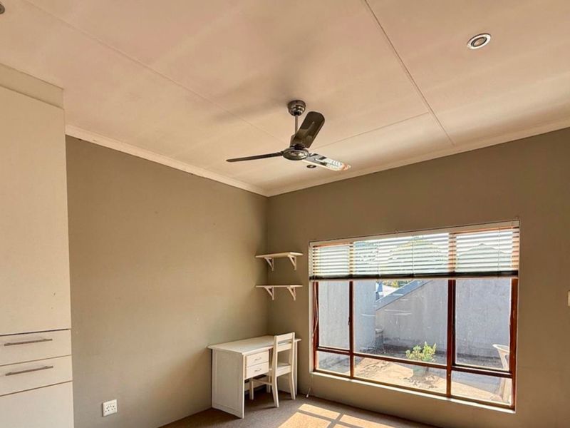 A bedroom featuring built-in cabinetry, a ceiling fan, recessed lighting, and a large window with venetian blinds, offering a functional and neutral living space.