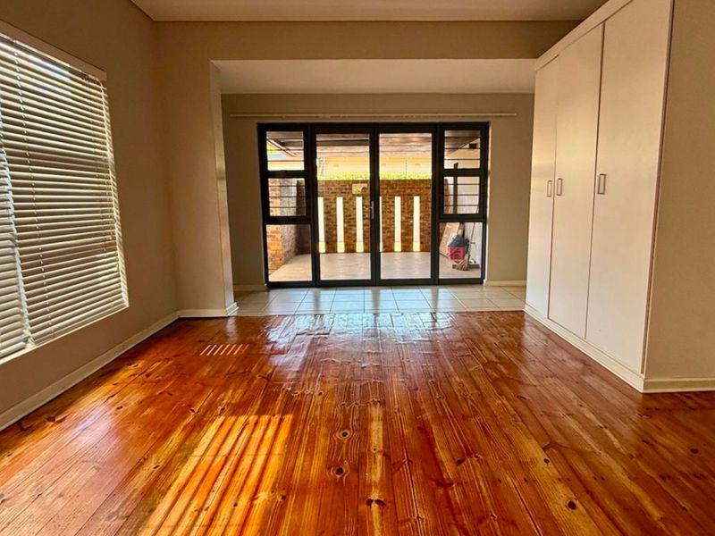 Spacious bedroom featuring polished timber flooring, built-in cupboards, and large aluminium sliding doors providing access to an outdoor patio area.