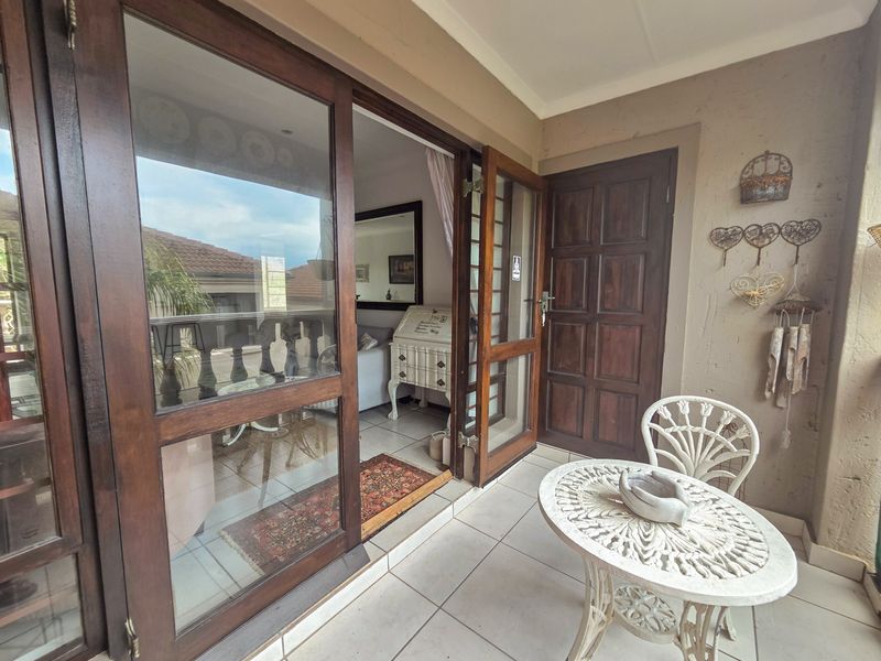 A covered balcony featuring tiled flooring and wooden door access to the interior living space.