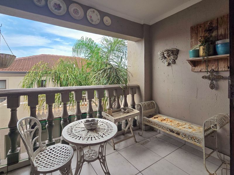 A covered balcony featuring a classic balustrade and tiled flooring, offering an outdoor space with views of the surrounding residential area.