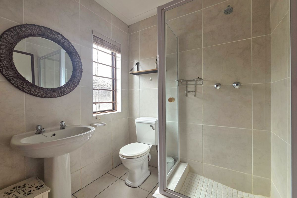 A functional bathroom featuring a pedestal washbasin, a toilet, and a glass-enclosed shower with neutral wall and floor tiling.