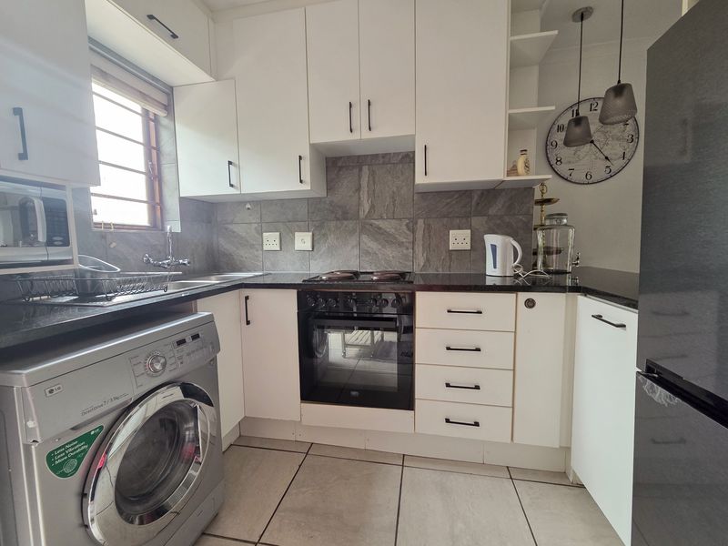 A well-maintained kitchen featuring white cabinetry, granite countertops, a tiled backsplash, and integrated appliances including an oven and hob.