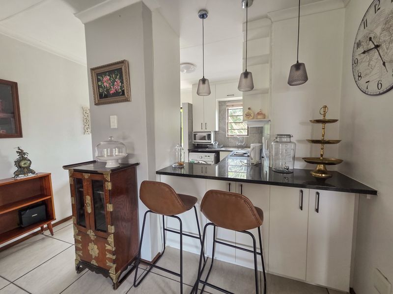 A functional kitchen featuring white cabinetry, dark granite countertops, a breakfast bar, and modern pendant lighting, seamlessly connected to the living area.