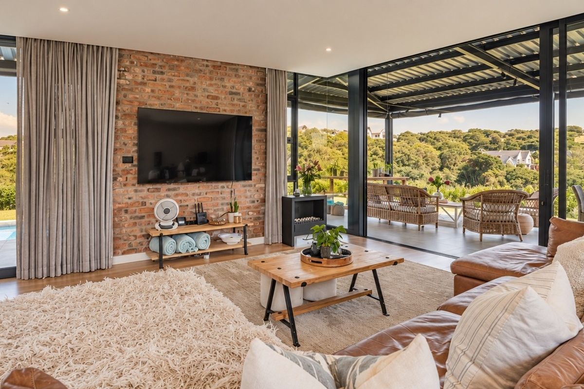 Spacious living room featuring an exposed brick feature wall, recessed lighting, and large sliding glass doors opening onto a covered patio with scenic views.