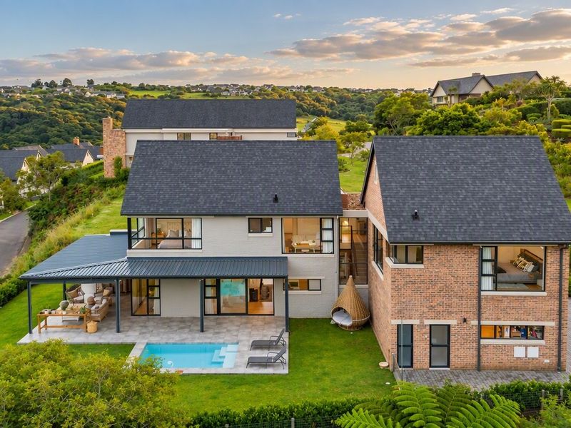 Aerial view of a modern two-story residential property featuring a swimming pool, covered patio, and landscaped garden in a scenic estate setting.