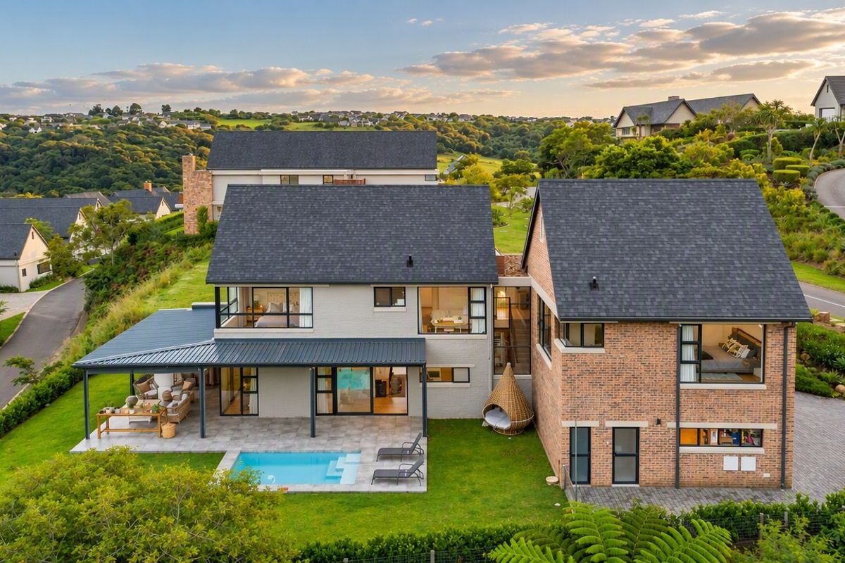 Aerial view of a modern two-story residential property featuring a swimming pool, covered patio, and landscaped garden in a scenic estate setting.