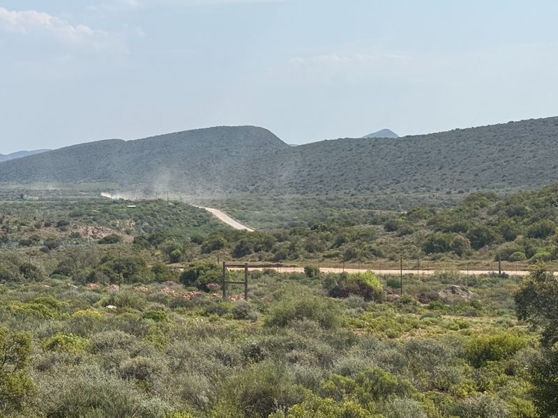 Expansive landscape view of the surrounding farm terrain, featuring rolling hills, natural vegetation, and a distant gravel access road.