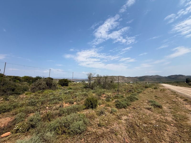 A view of the farm property boundary featuring wire fencing along a dirt road with expansive mountain landscape in the background.