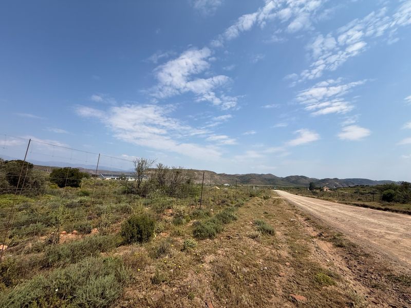 A view of the gravel access road leading to the farm property, bordered by wire fencing and natural landscape.
