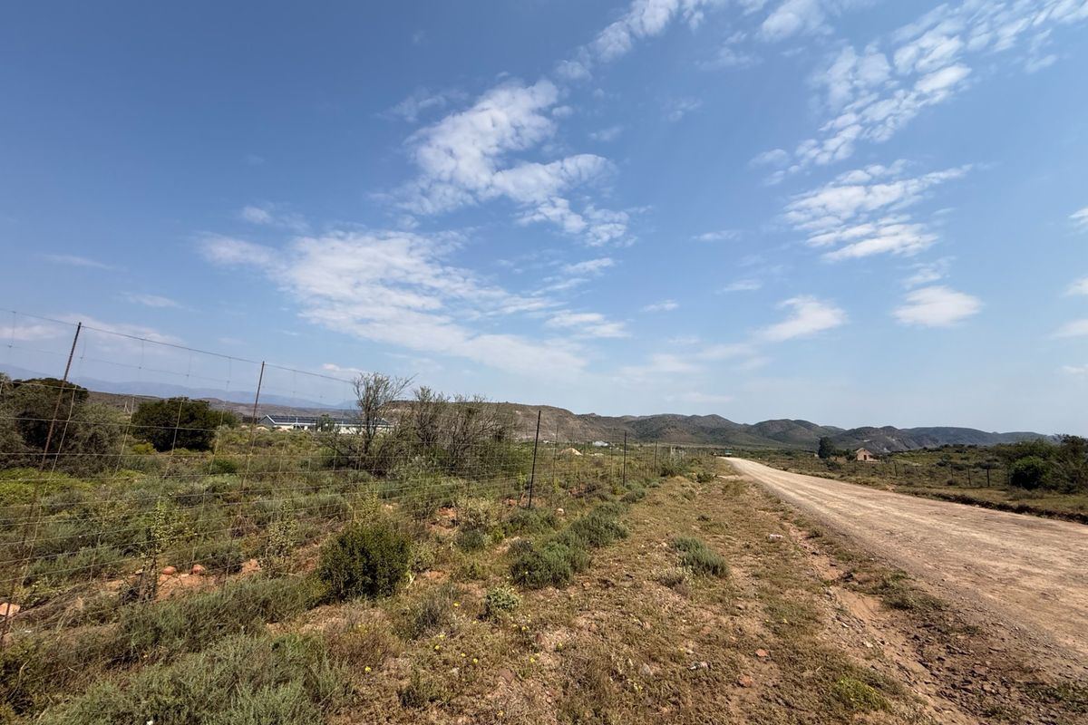 A view of the gravel access road leading to the farm property, bordered by wire fencing and natural landscape.
