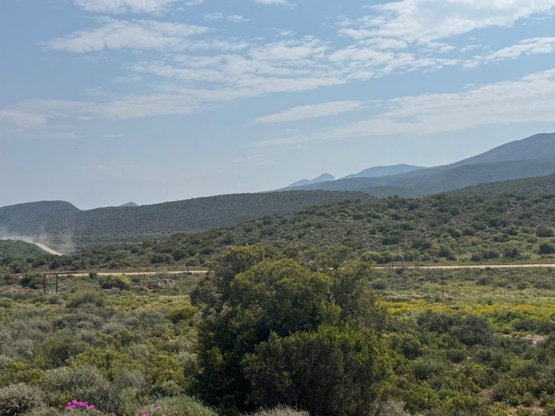 Expansive landscape view featuring rolling hills, natural vegetation, and a distant dirt road, showcasing the rural character of the farm property.