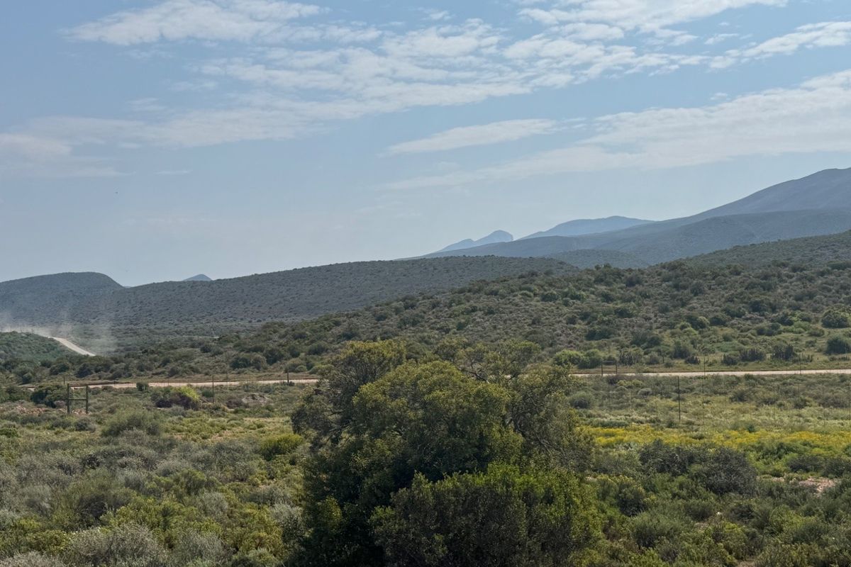 Expansive landscape view featuring rolling hills, natural vegetation, and a distant dirt road, showcasing the rural character of the farm property.
