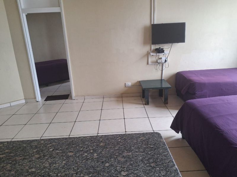 A bedroom featuring tiled flooring and a doorway leading to an adjacent space, with visible wall wear and exposed electrical wiring.