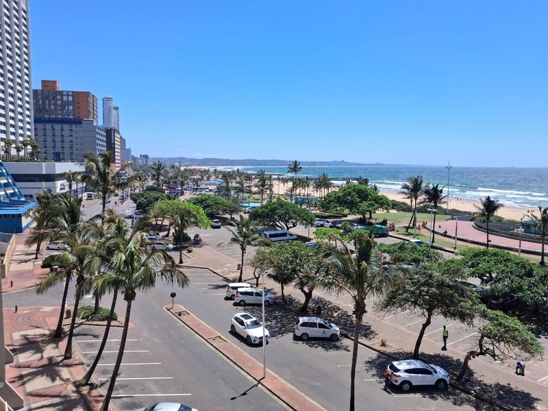 Elevated panoramic view overlooking the coastal beachfront, public parking area, and surrounding urban cityscape.