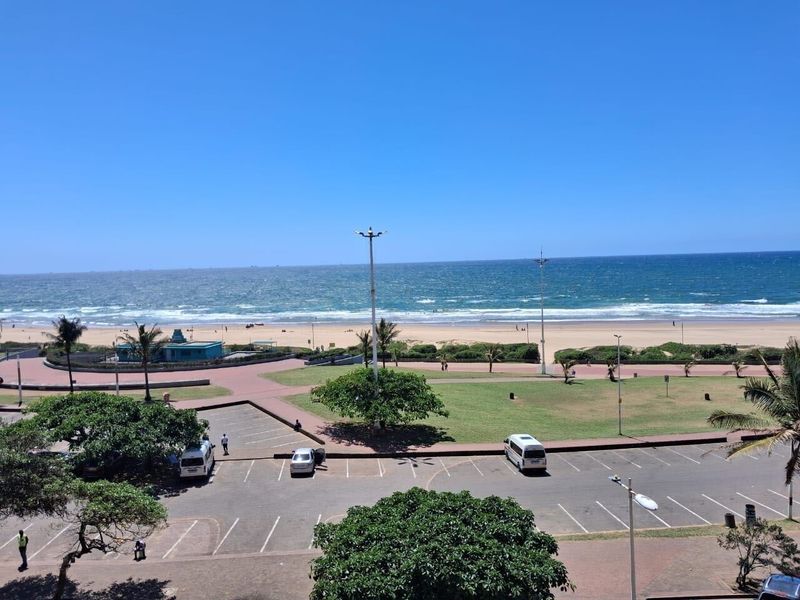 A clear, elevated view overlooking the beach, ocean, and adjacent public parking and park area.