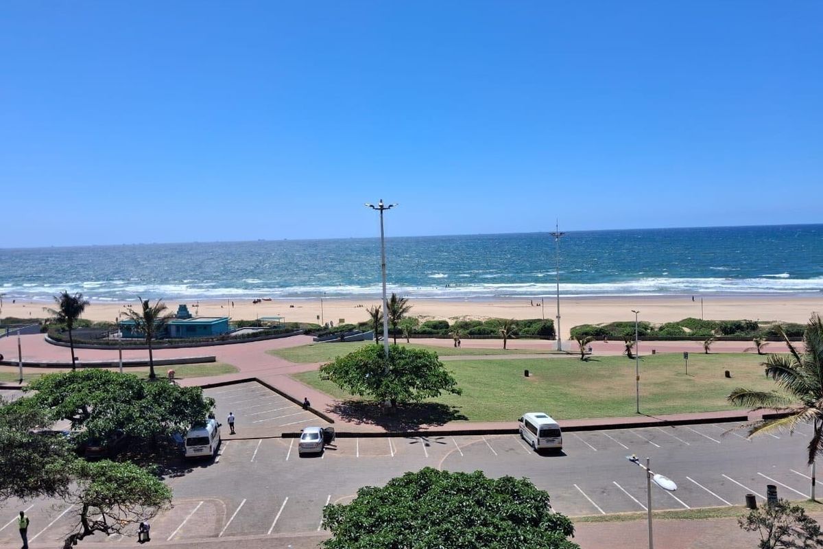 A clear, elevated view overlooking the beach, ocean, and adjacent public parking and park area.