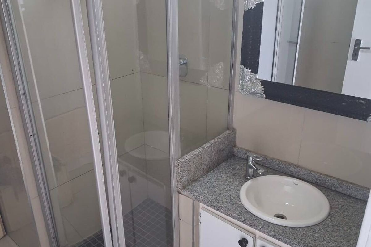 A functional bathroom featuring a glass shower enclosure, a granite-topped vanity with a drop-in basin, and neutral wall tiling.
